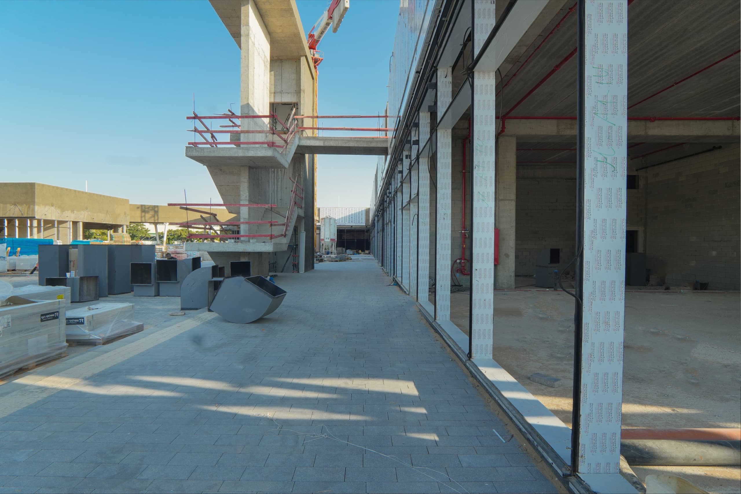 מבט לאורך שדרת החנויות בשלד המתחם — שורת עמודים, חזיתות זכוכית וקו פרספקטיבה אל עומק המעבר