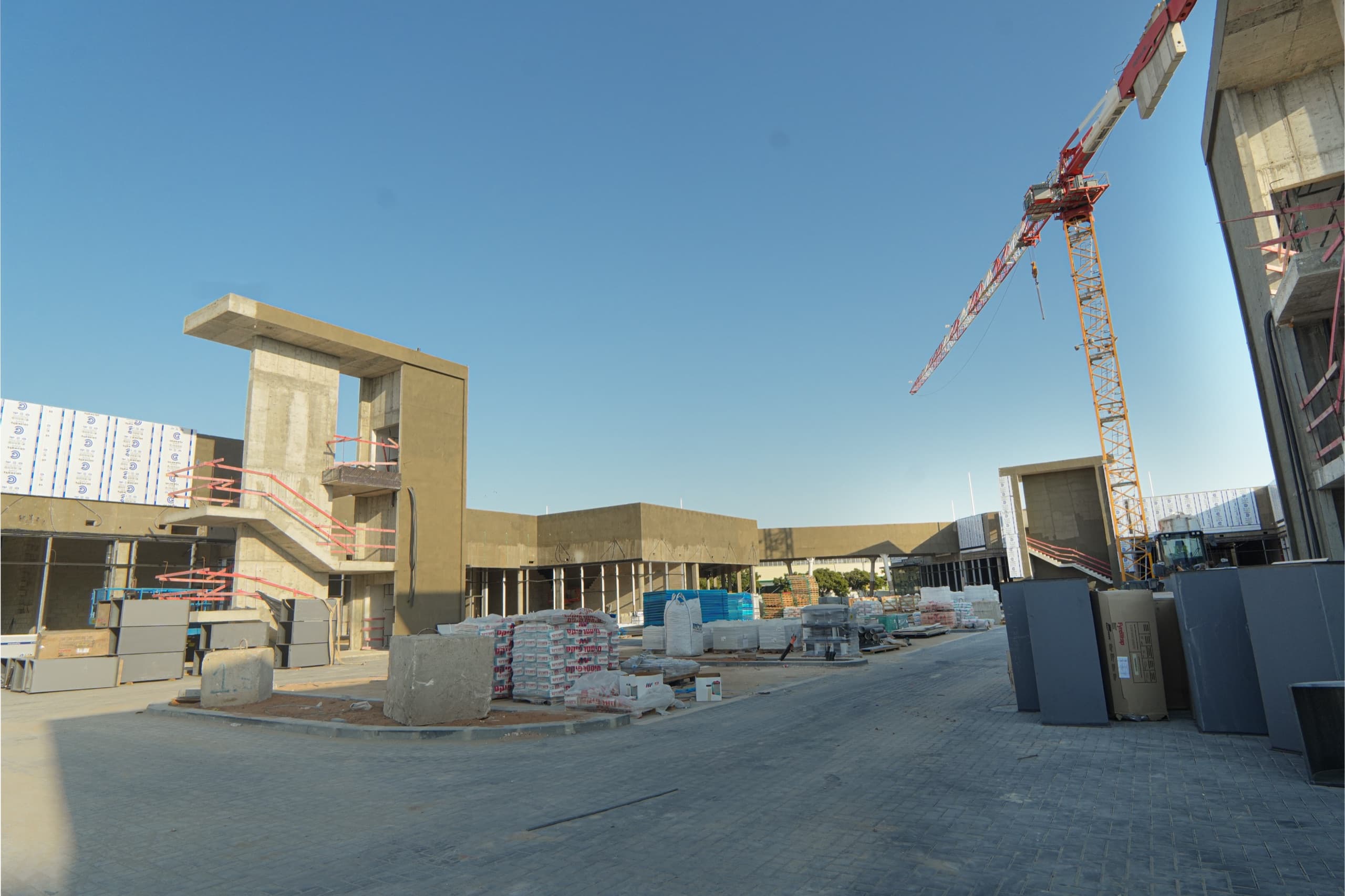 ציר התנועה הפנימי של המתחם בשעת אחר צהריים, עם מגדל בטון וחומרי בנייה לאורך הדרך